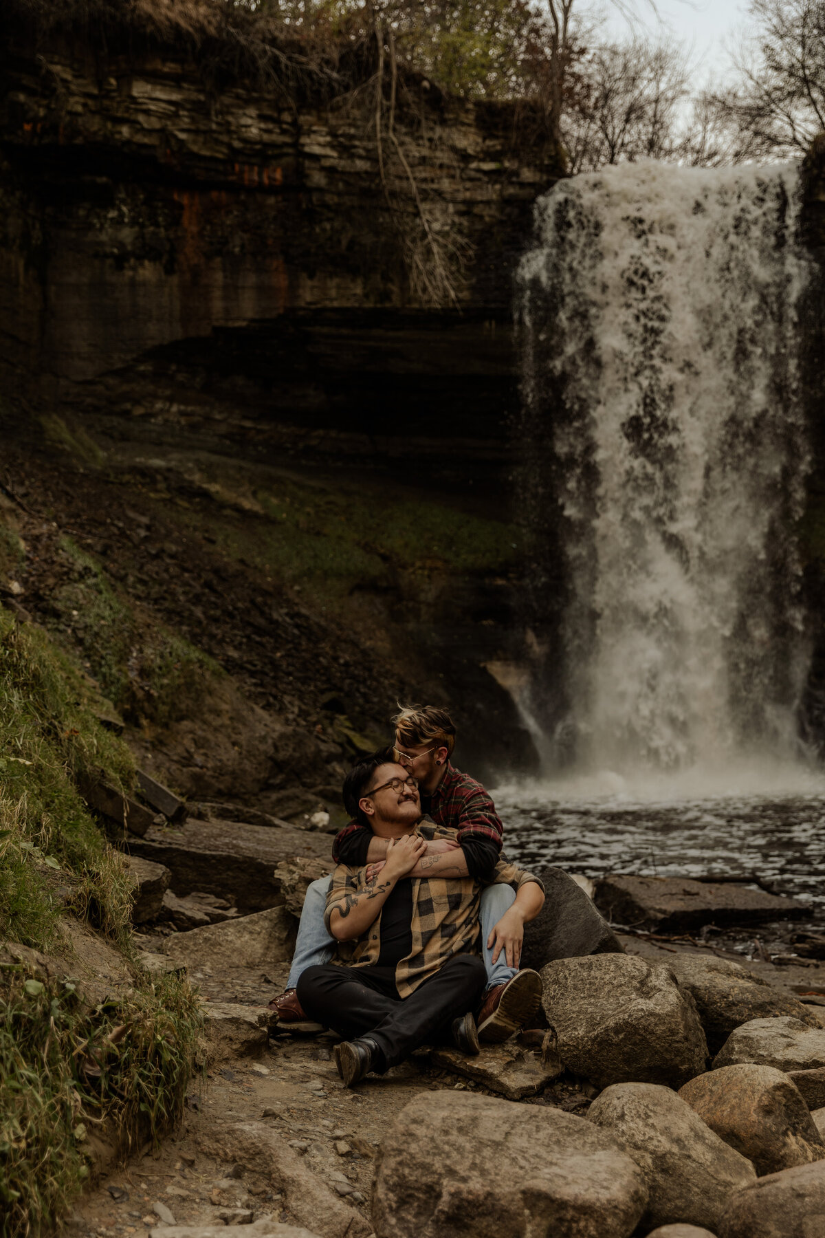 Queer couple sitting in front of Minnehaha Falls for their couples photos 