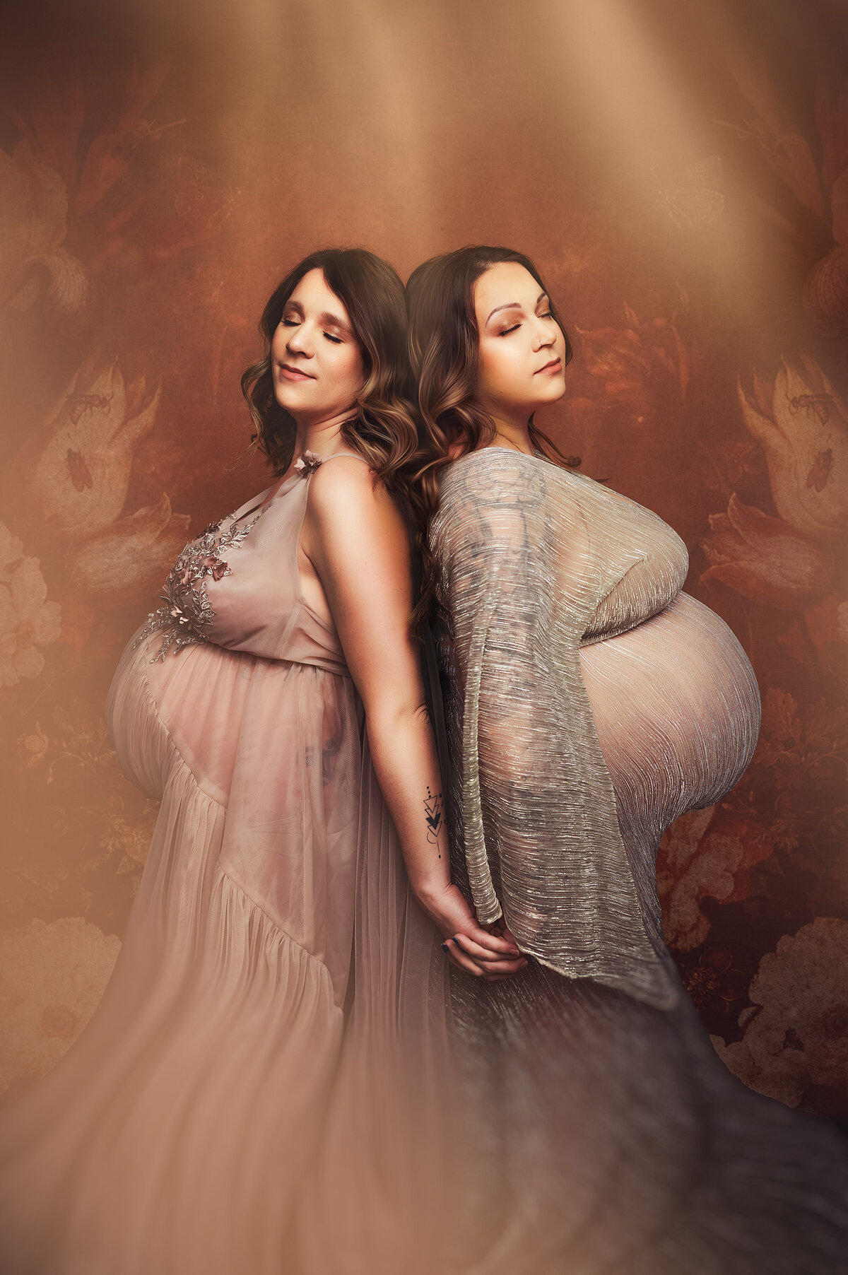Pregnant twin women lean into each other, wearing gowns from our client closet.