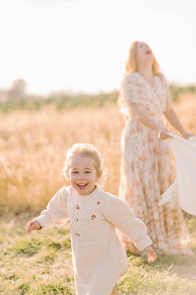 Young girl running away from her laughing mother who is holding a blanket