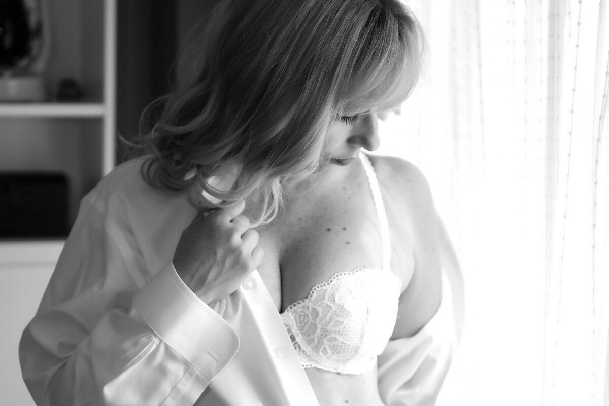 boudoir photo of woman in mens white shirt with white lacy bra peeking through