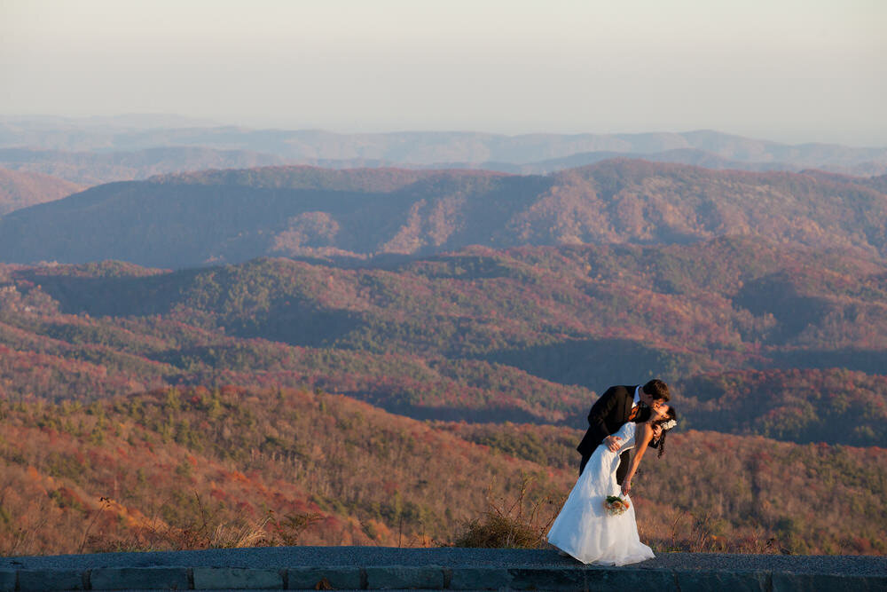 groom dips and kisses his bride in front of the blue ridge mountains