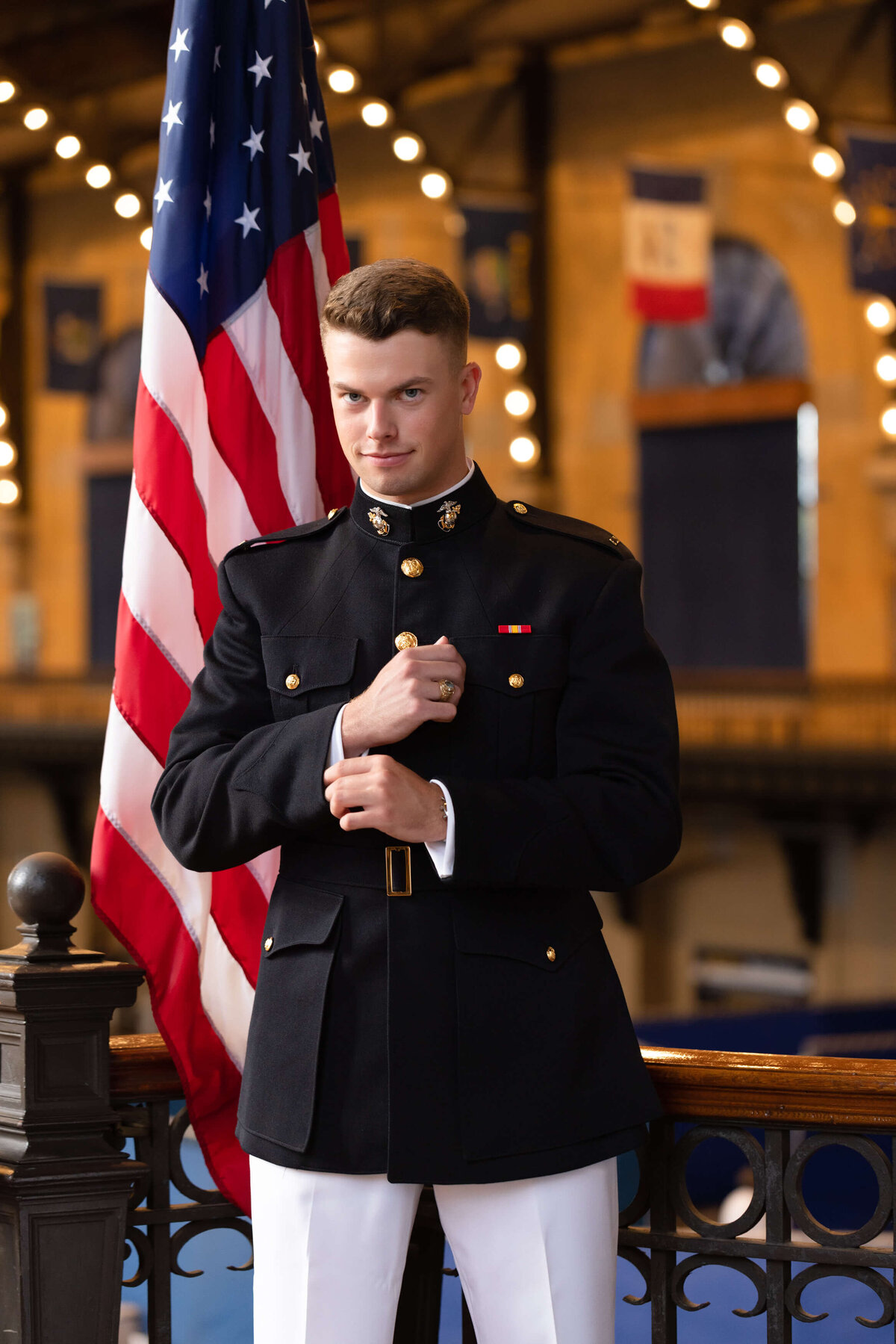 Midshipman smiles in front of American flag in Dhalgren Hall at the Naval Academy during senior photography session Kelly Eskelsen.