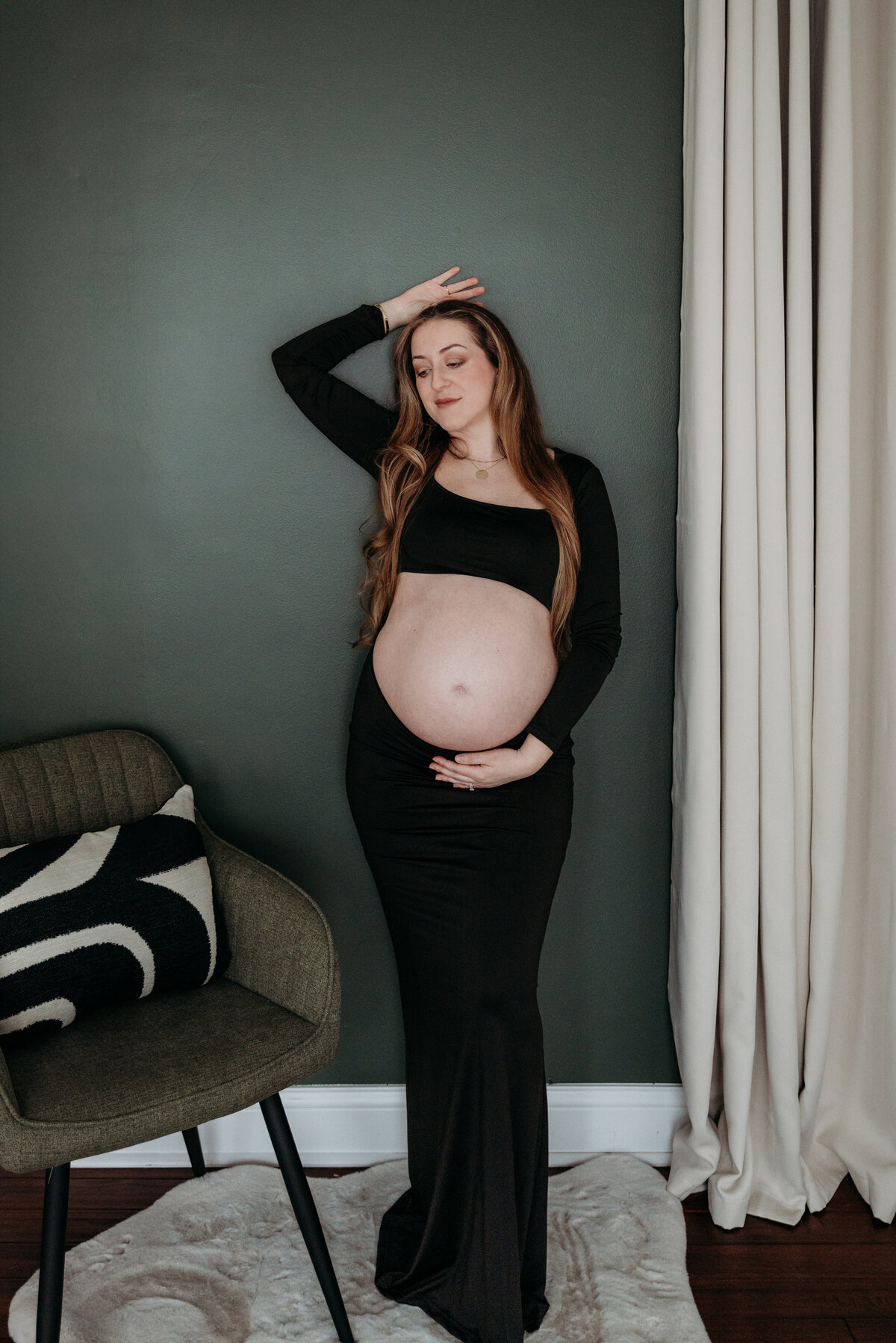 Pregnant mom leaning against a green wall as she embraces her baby bump imagining the days to come, during a studio maternity photoshoot in Bartlett, IL