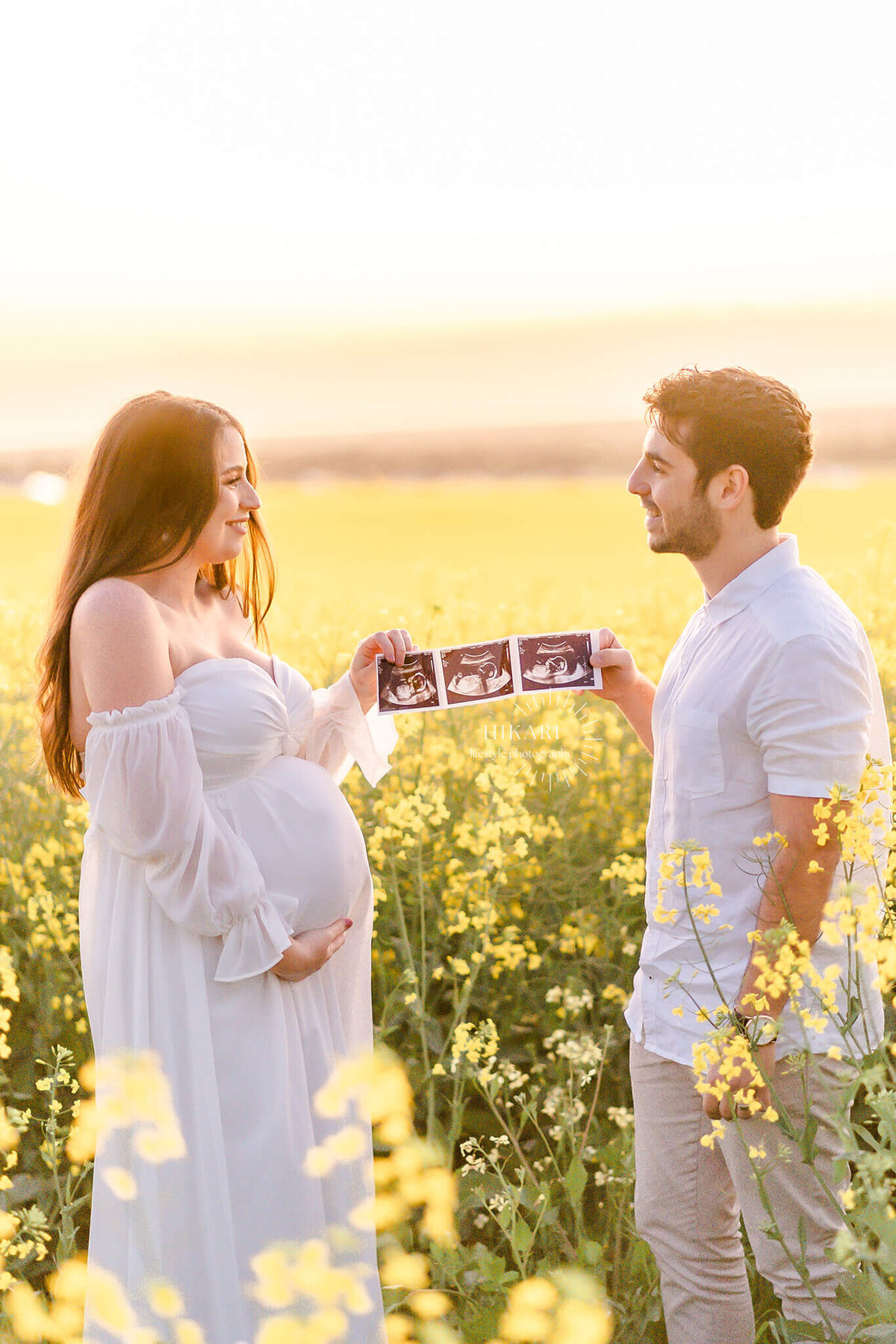 couple holding baby ultrasound smiling at each other in canola field SA during maternity photoshoot