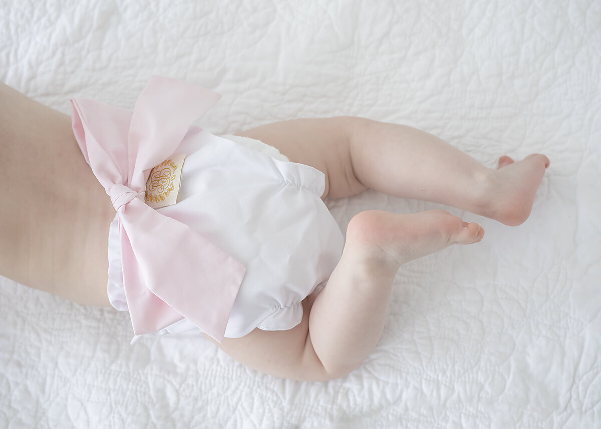 baby girl photographed in studio wearing a beaufort bonnet company diaper cover with pink bow