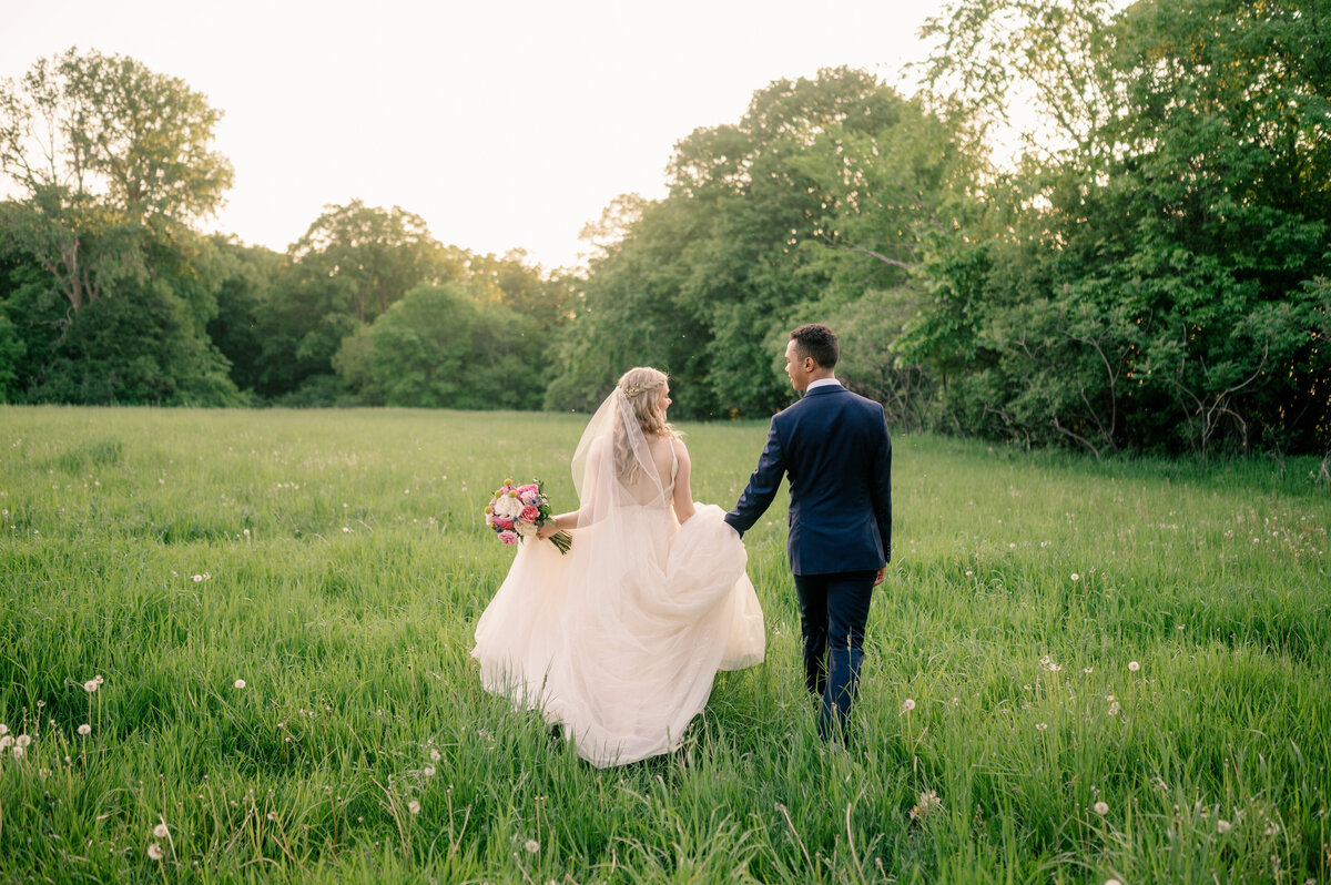 Bride and groom standing in tall grass and trees while holding hands