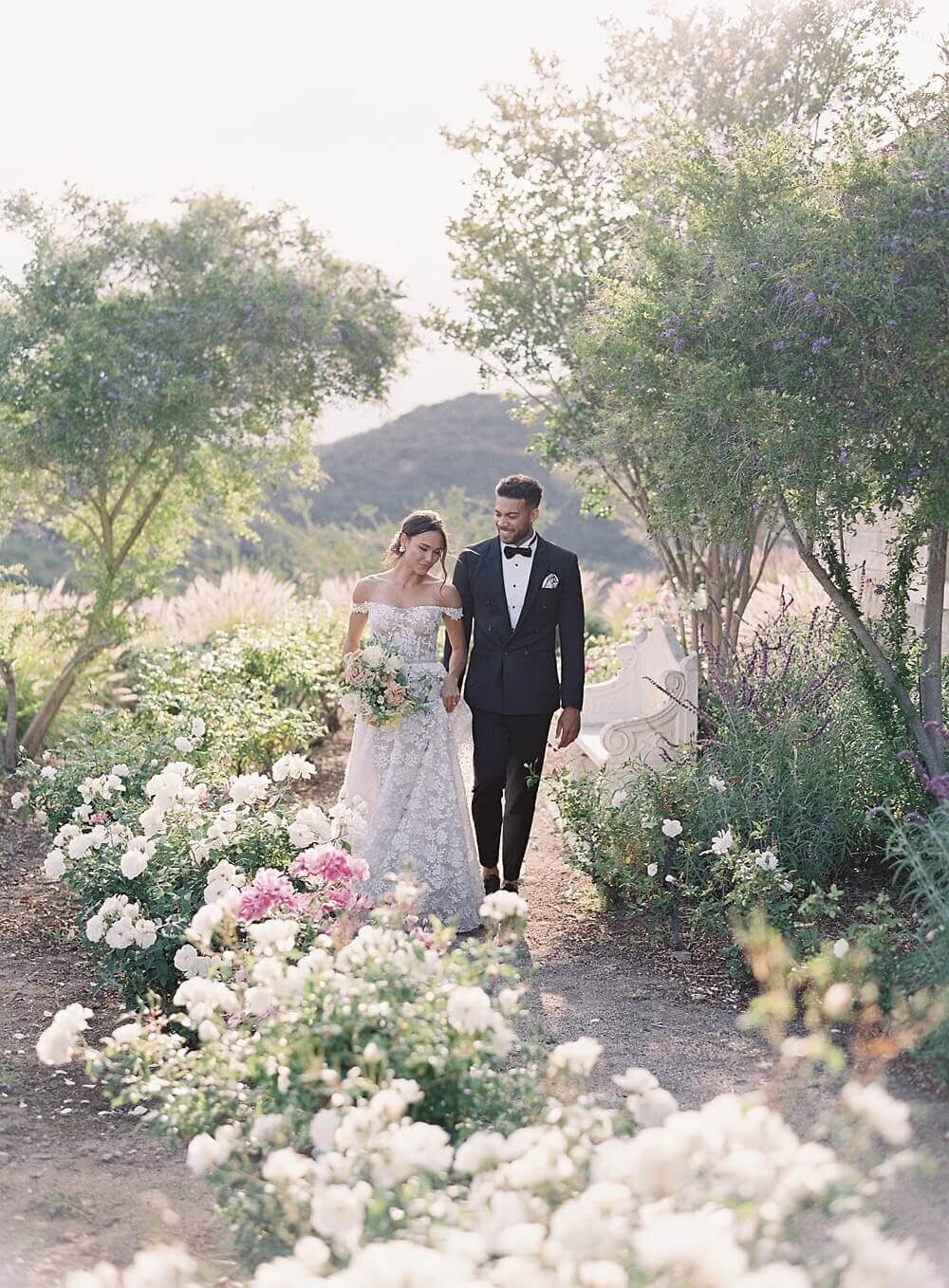 bride and groom walk through rose garden at cal-a-vie wedding