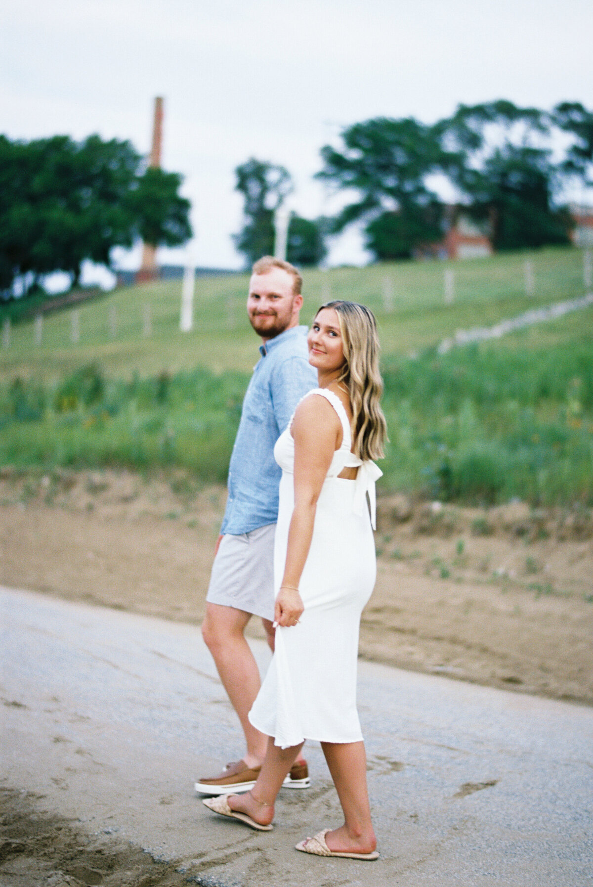 Couple walking at Edgewater Beach with bride smiling back during engagement session

