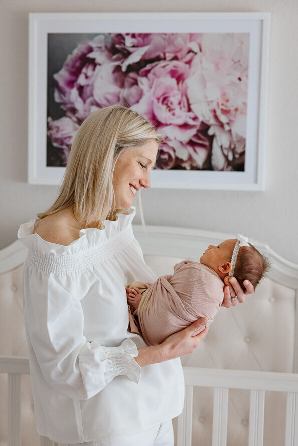 New mom smiles at her newborn baby in a pink nursery.