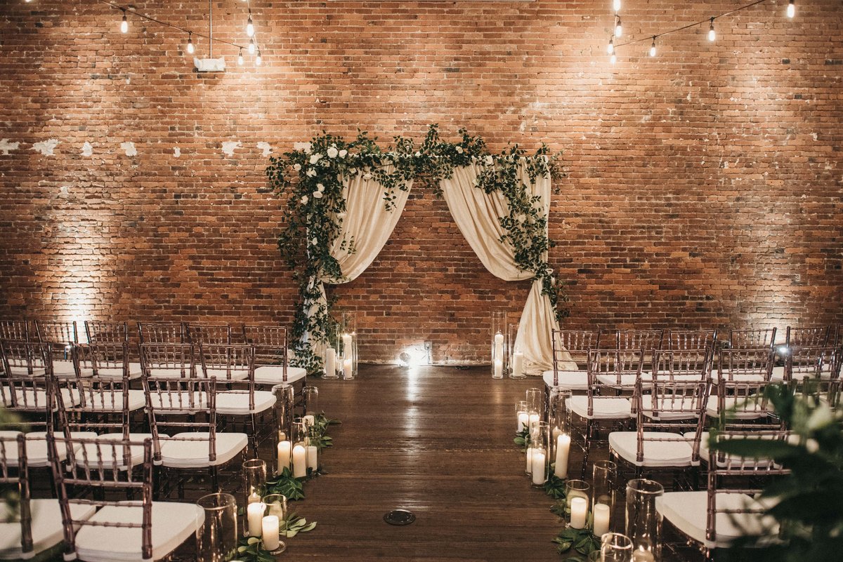 Axis Pioneer wedding with draped wedding arbor covered in greenery and aisle lined in candles