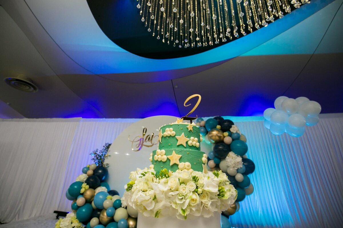 Green and white birthday cake with white flowers and balloon backdrop