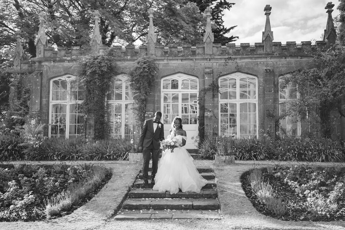 Black and white image of bride and groom outside the orangery at St Audries Park, they are walking down the steps hand in hand and are looking down. The bride is holding her boquet.
