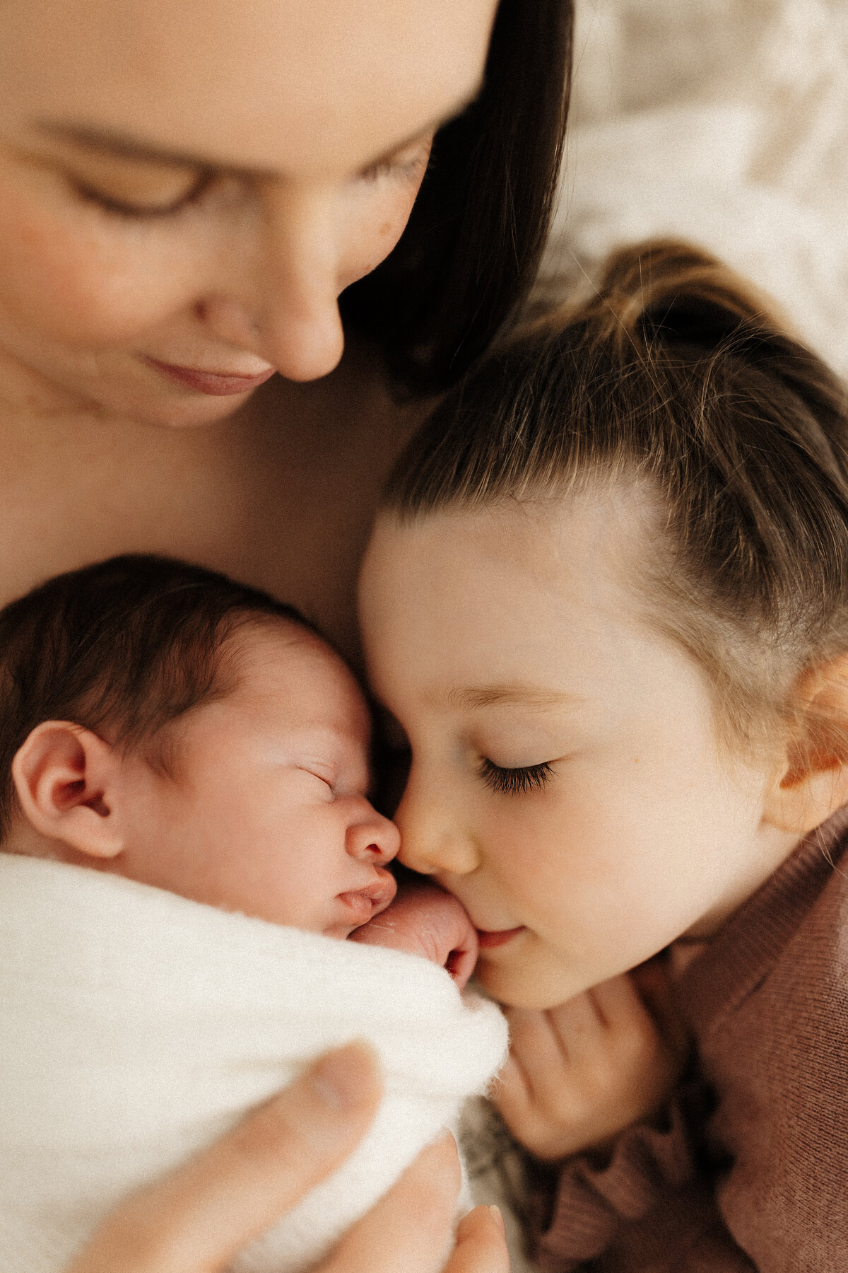 A sister kissing her newborn siblings hand while her mother looks on during a newborn photoshoot with christchurch photographer lucy jane photography