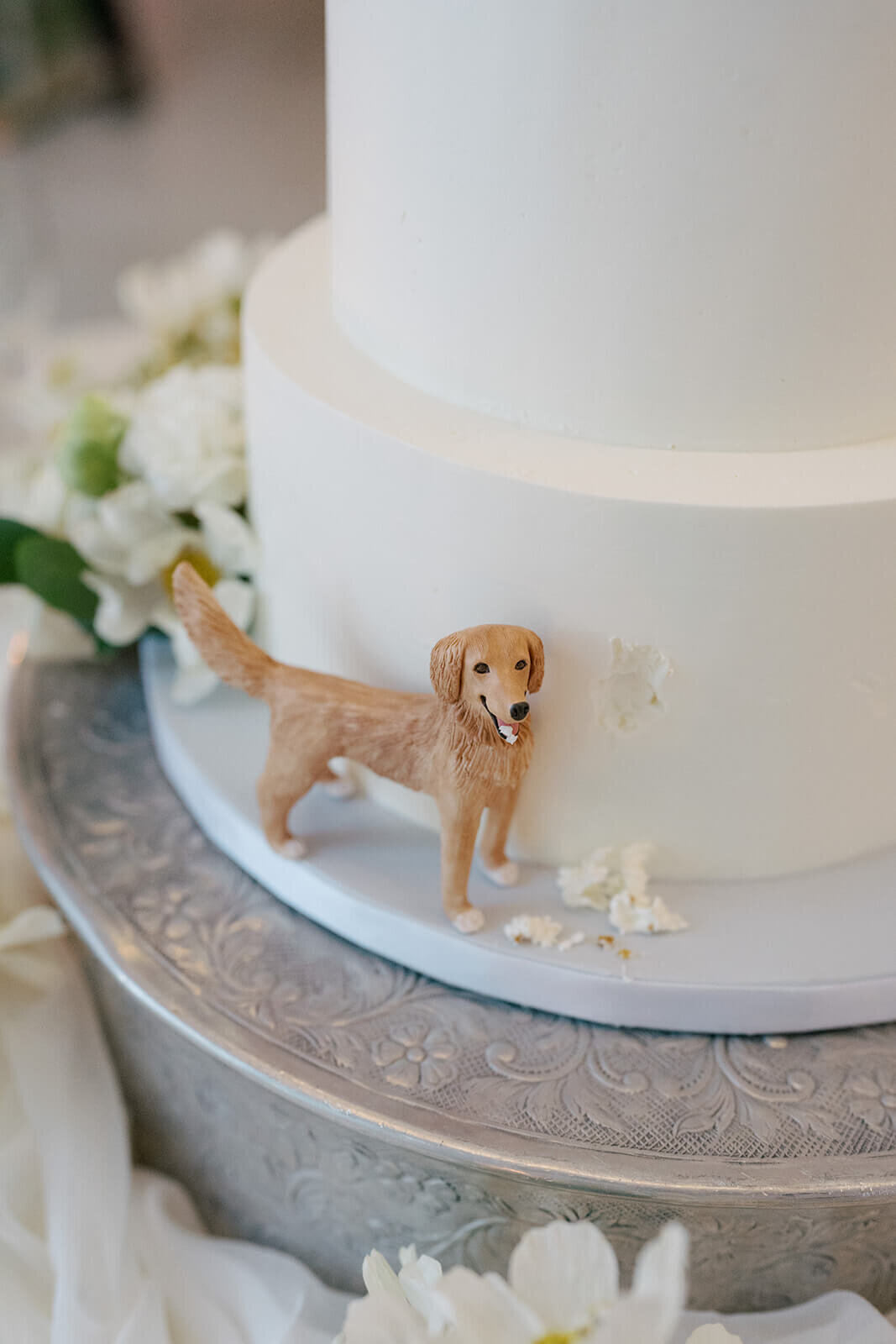 Wedding cake at the Aspen Meadows Resort wedding reception features a figurine of their pet dog golden retriever taking a small bite of the wedding cake.