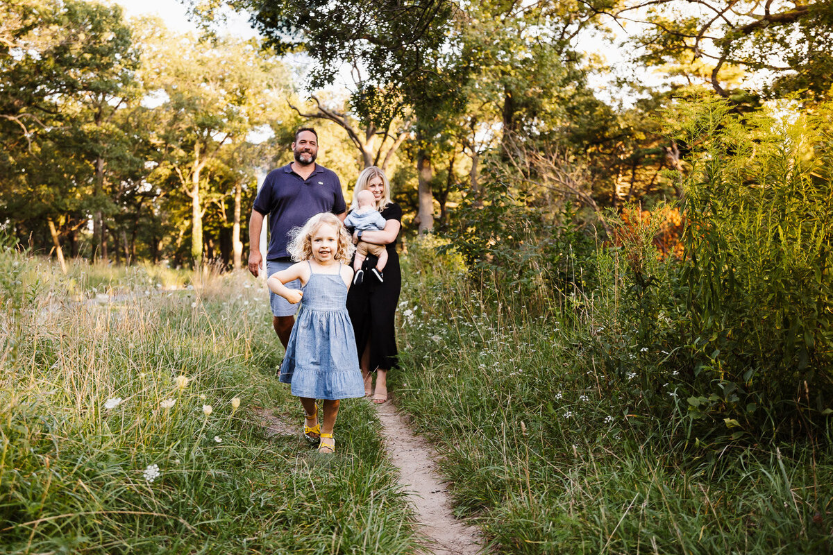 Little girl leading her family through park path during family photos by Claire Binks Photography