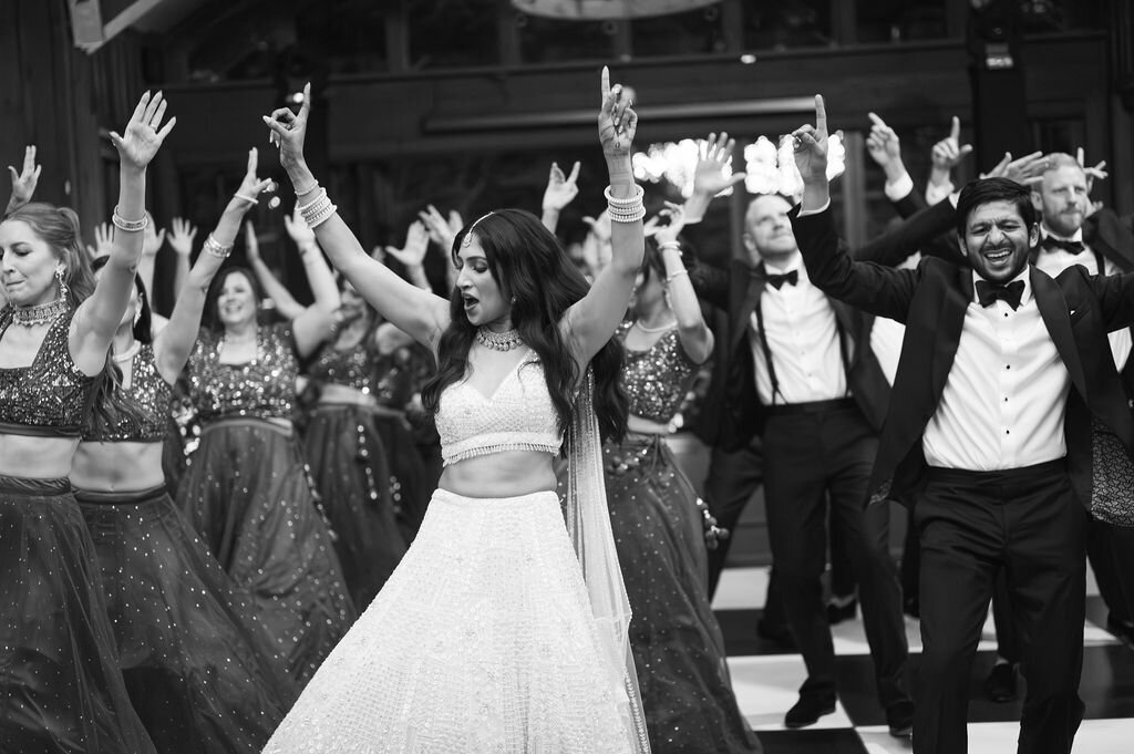 Bride leading a choreographed group dance surrounded by guests beneath chandeliers at a luxury mountain wedding reception.