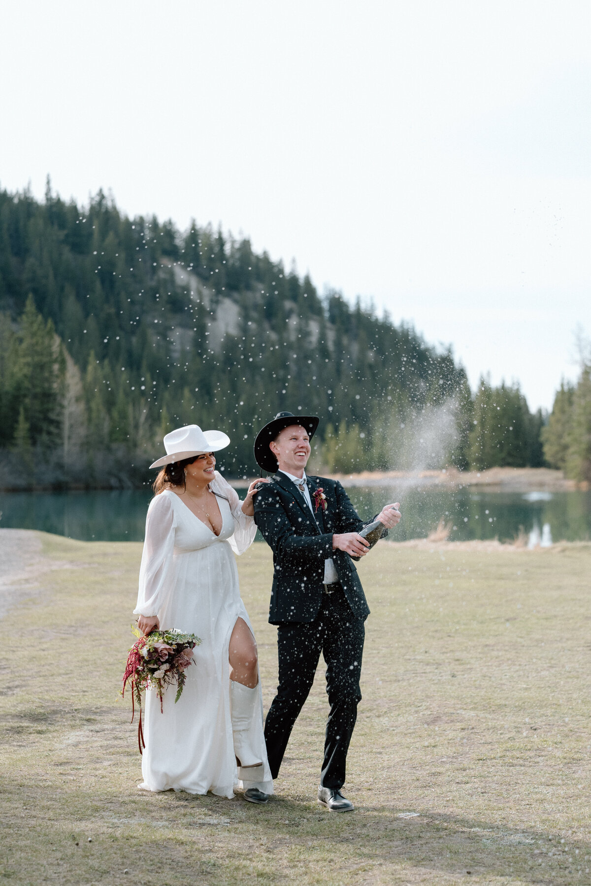Couple popping champagne during post-wedding celebration in the Banff wilderness.