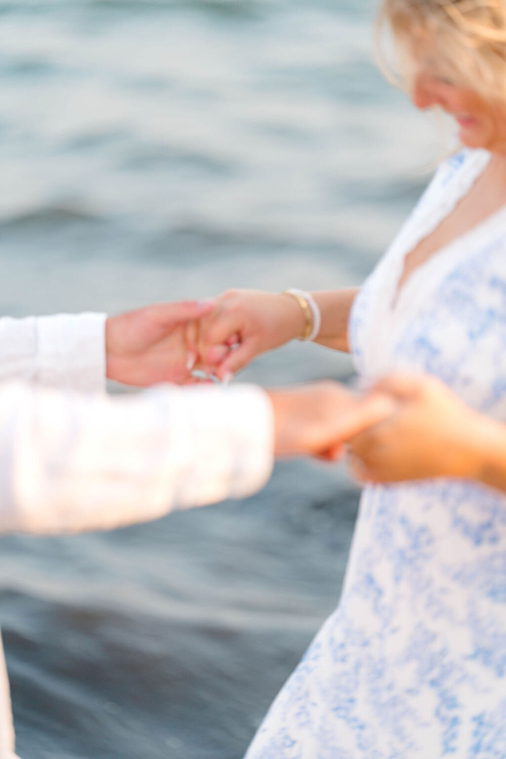 Newport Rhode Island Engagement Photo Photographer | Two people holding hands near water, with one in a white and blue dress. 