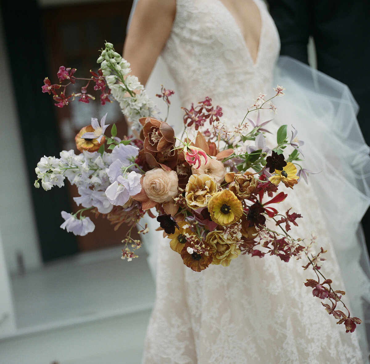 Organic artistic bridal bouquet with delicate blooms and texture. Fall bridal bouquet for private home wedding featuring orchids, ranunculus, and sweet peas. Textural bridal bouquet in a tasteful fall pallet of copper, lavender, gold, and ruby. Private property autumnal wedding in the hills of Tennessee. Design by Rosemary & Finch Floral Design in Nashville, TN.