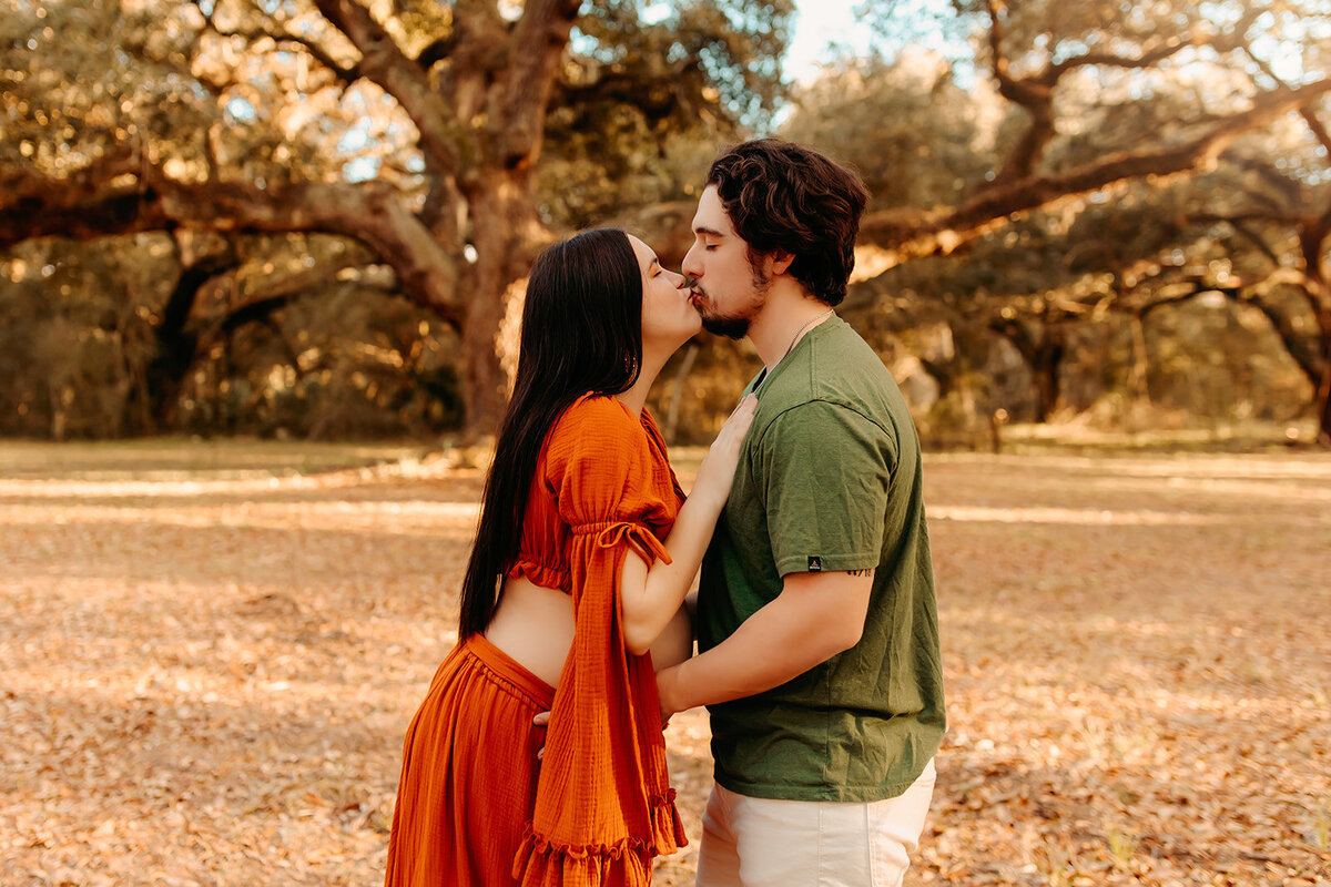 Couple maternity session in The Woodlands TX—expecting parents kissing under oak tree