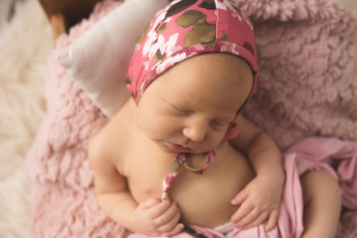 Newborn baby girl, wearing floral bonnet sleeping in tiny bed during newborn photoshoot in Franklin tennessee photography studio