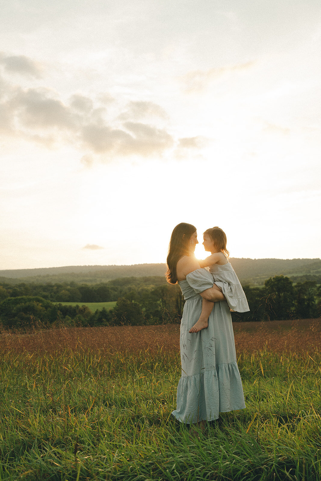 Pregnant mom holding her toddler in a field during a golden-hour maternity and motherhood session
