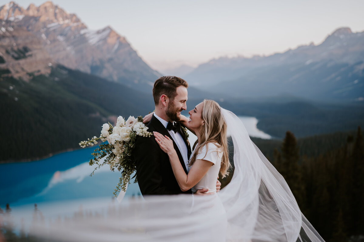 Couple with veil and white flowers look at each other during Banff elopement