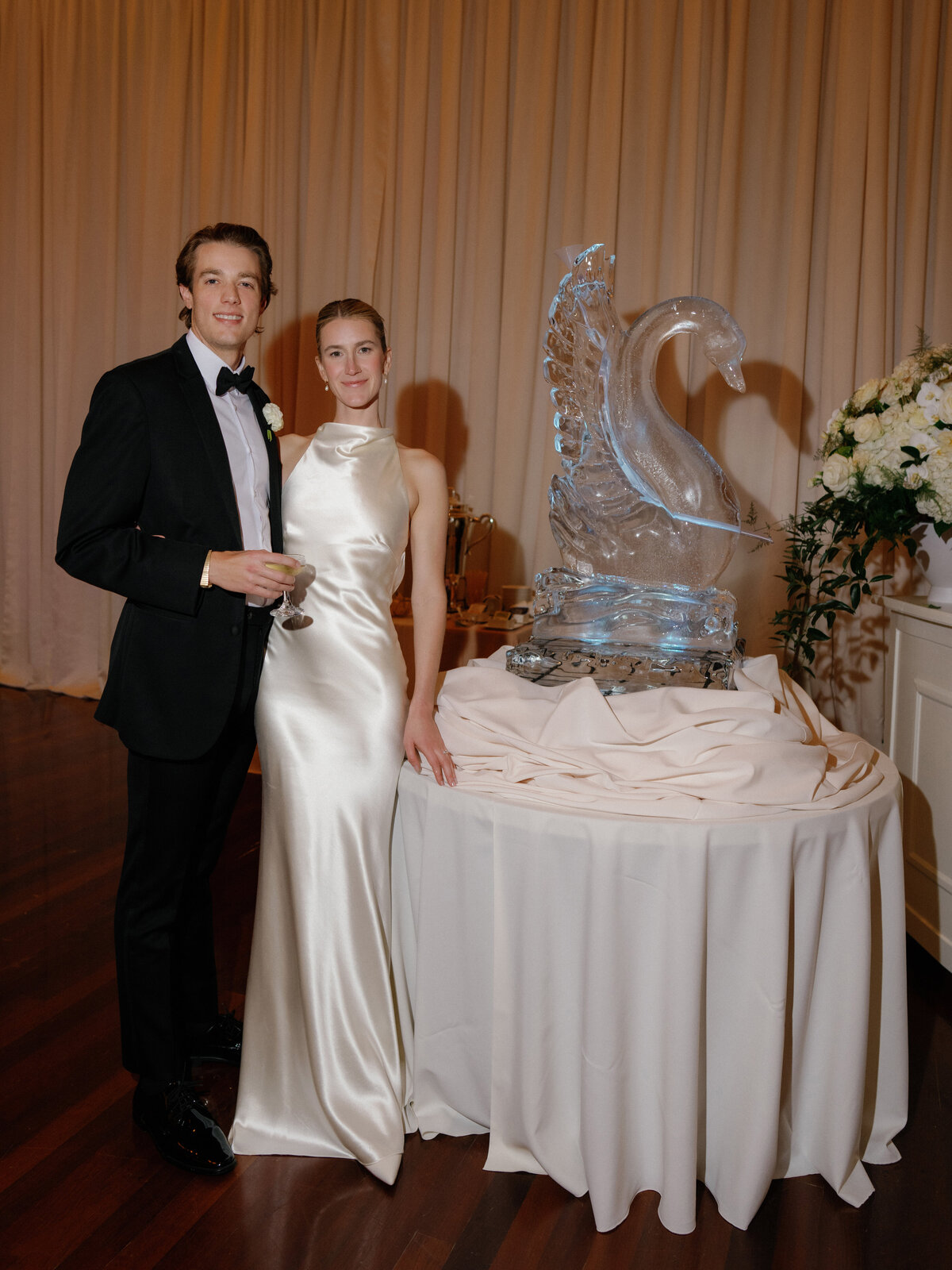 Bride and groom standing next to a swan ice sculpture