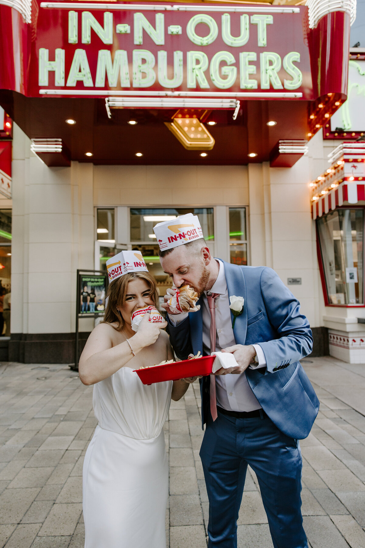 A couple holds In-N-Out burgers to their mouths on their elopement day in Vegas.