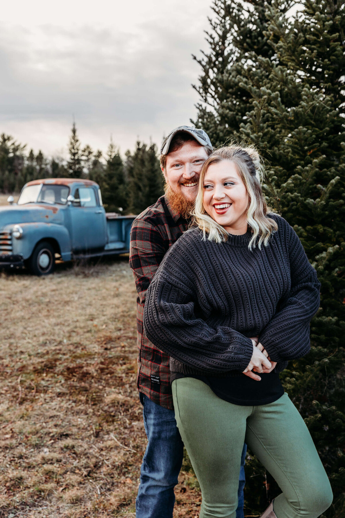 husband and wife hugging at a christmas tree farm for photo session