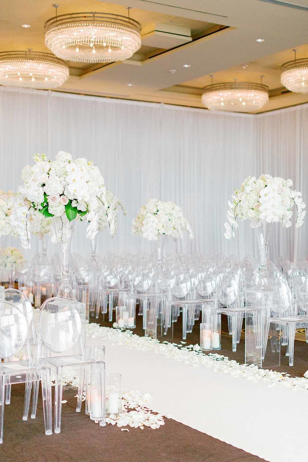 large orchid arrangements for wedding ceremony with white rose petals, white aisle runner, and clear lucite chairs