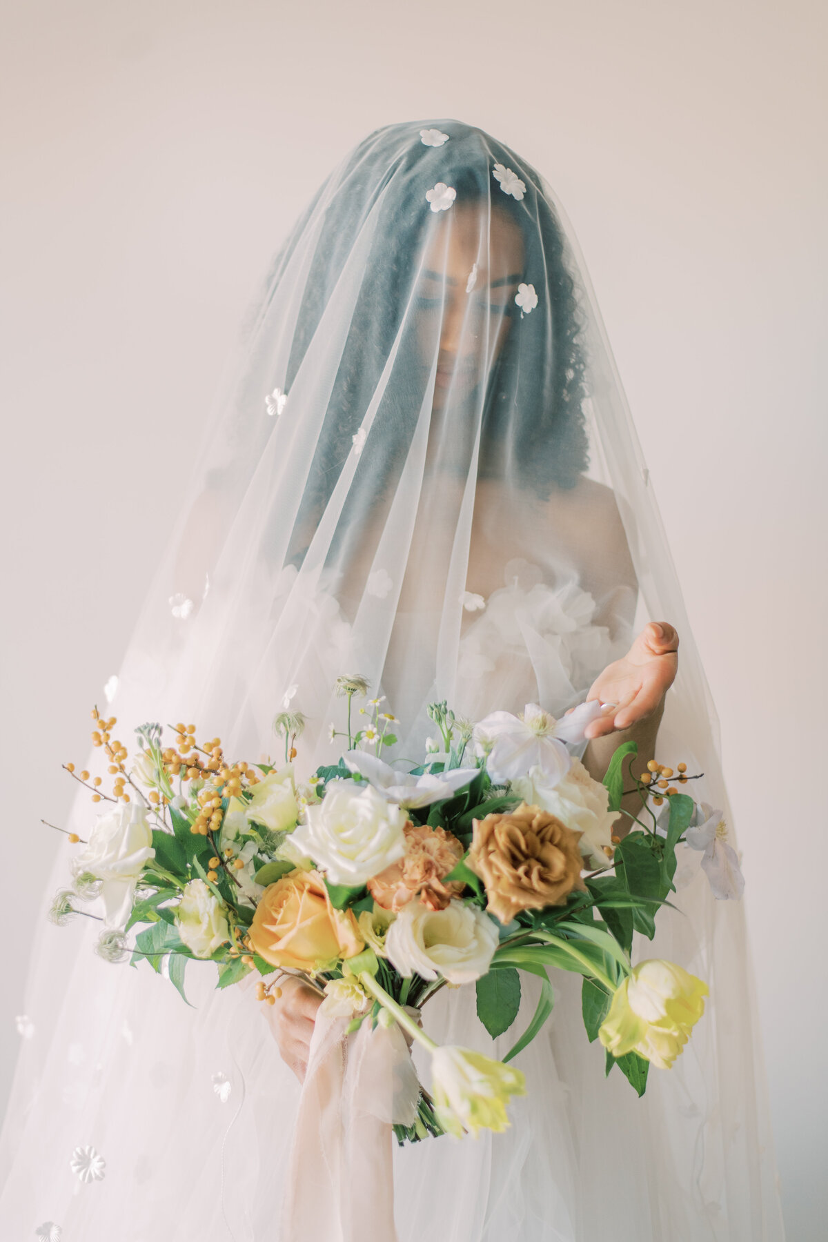 A bride standing serenely with her veil flowing, holding a lush bouquet of white and golden blooms, captured by Christine Grace Photography in Toronto.