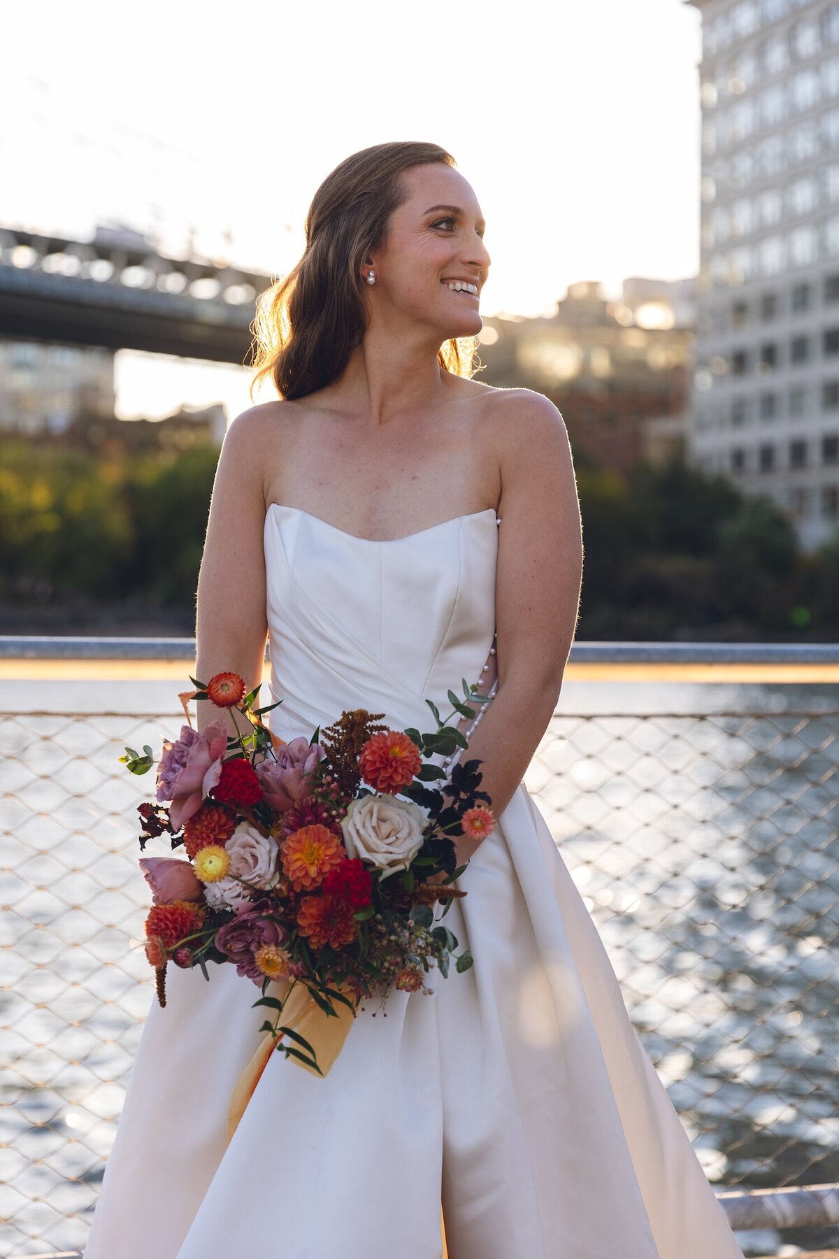 Bride smiling with bouquet by waterfront at sunset