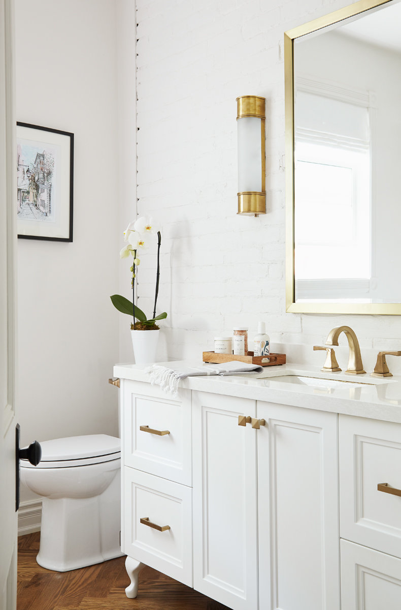 white bathroom with painted brick wall and gold interior fixtures