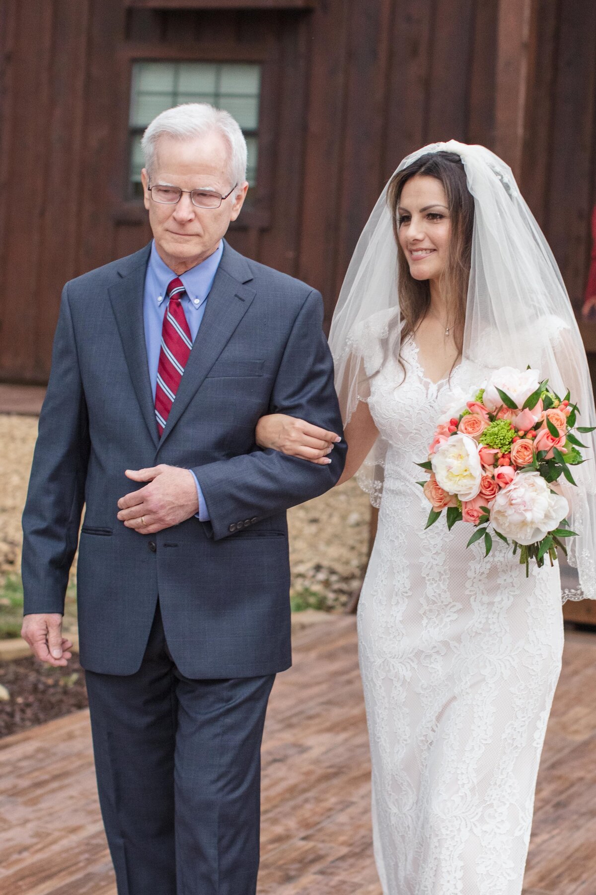 bride holds fathers arm while walking down the aisle with peach rose bouquet in Boerne Texas
