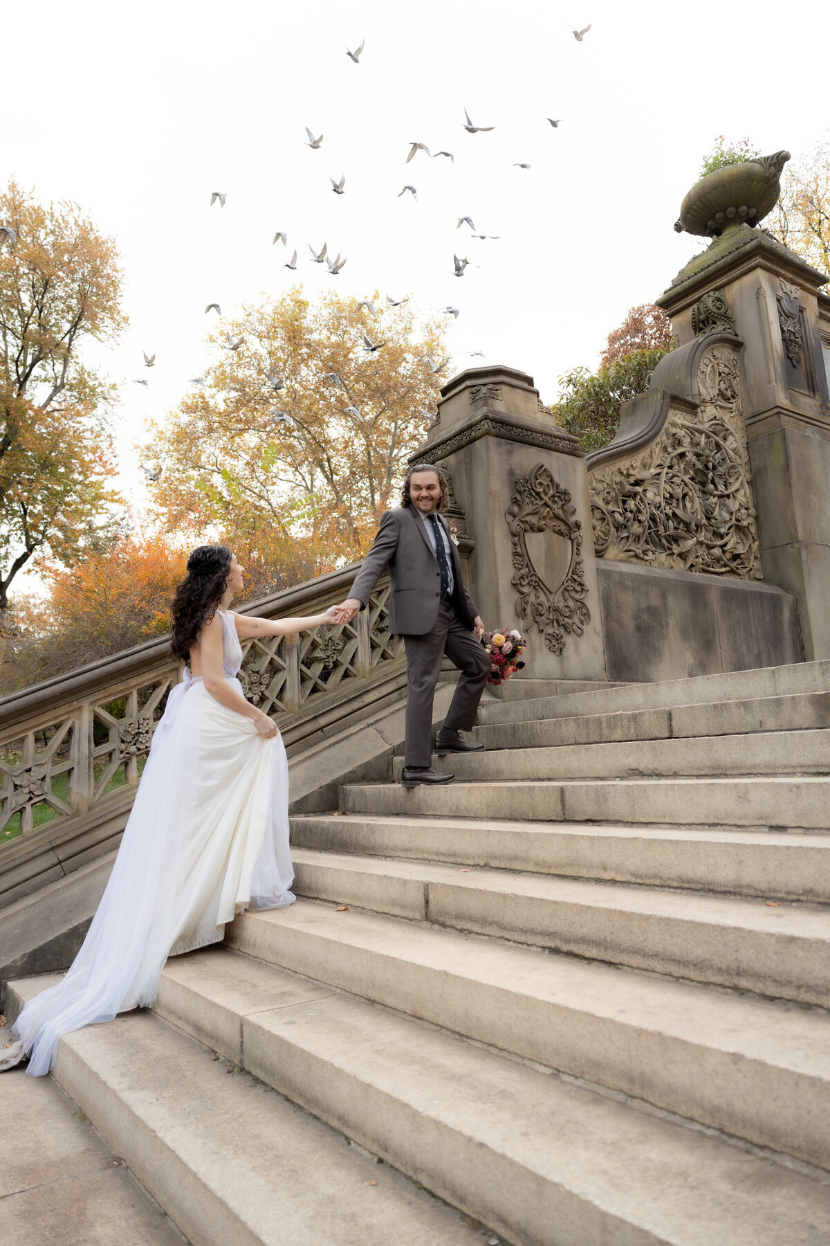 Bride and groom walking up the steps in Central Park, NYC, as birds fly around them during their fall elopement.