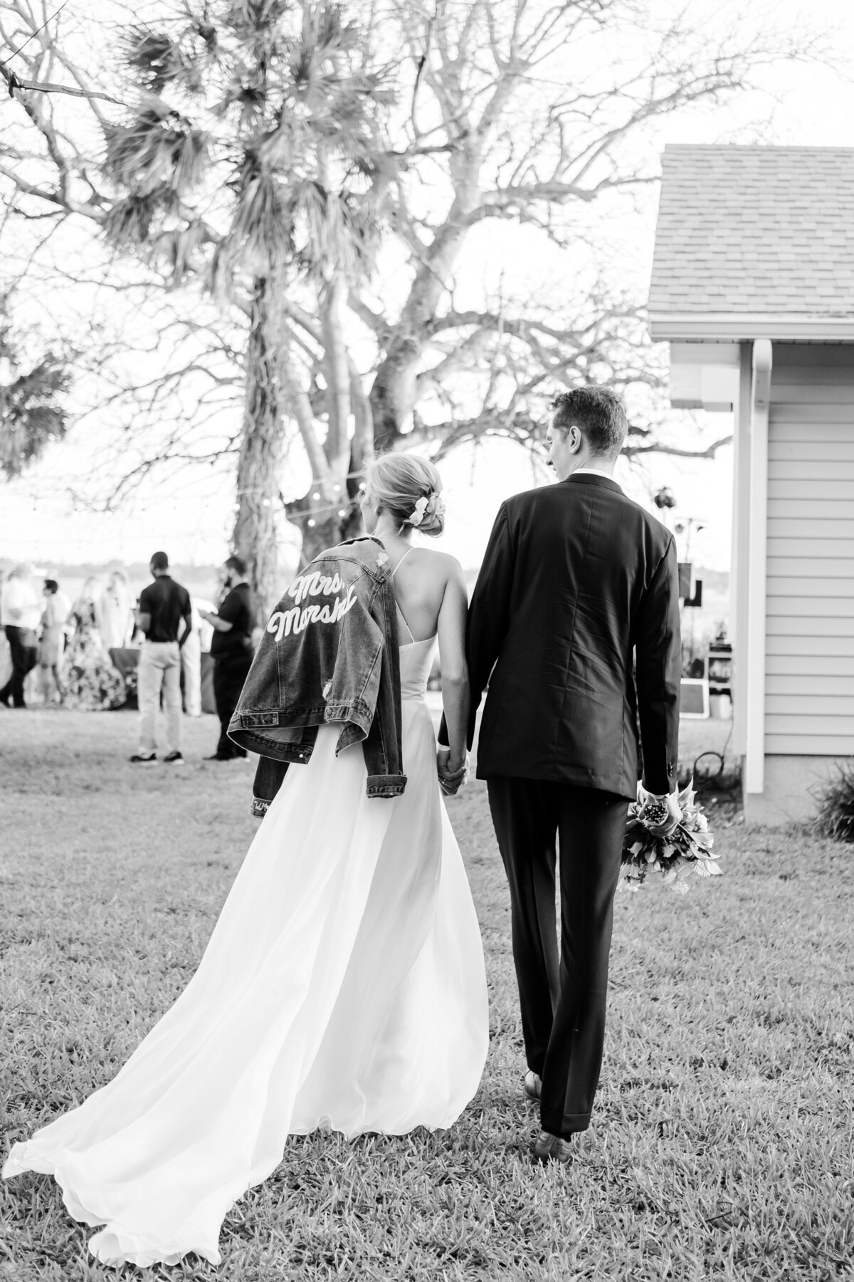 Bride holds custom denim jacket as her and her Groom walk into their wedding reception in Palmetto, FL