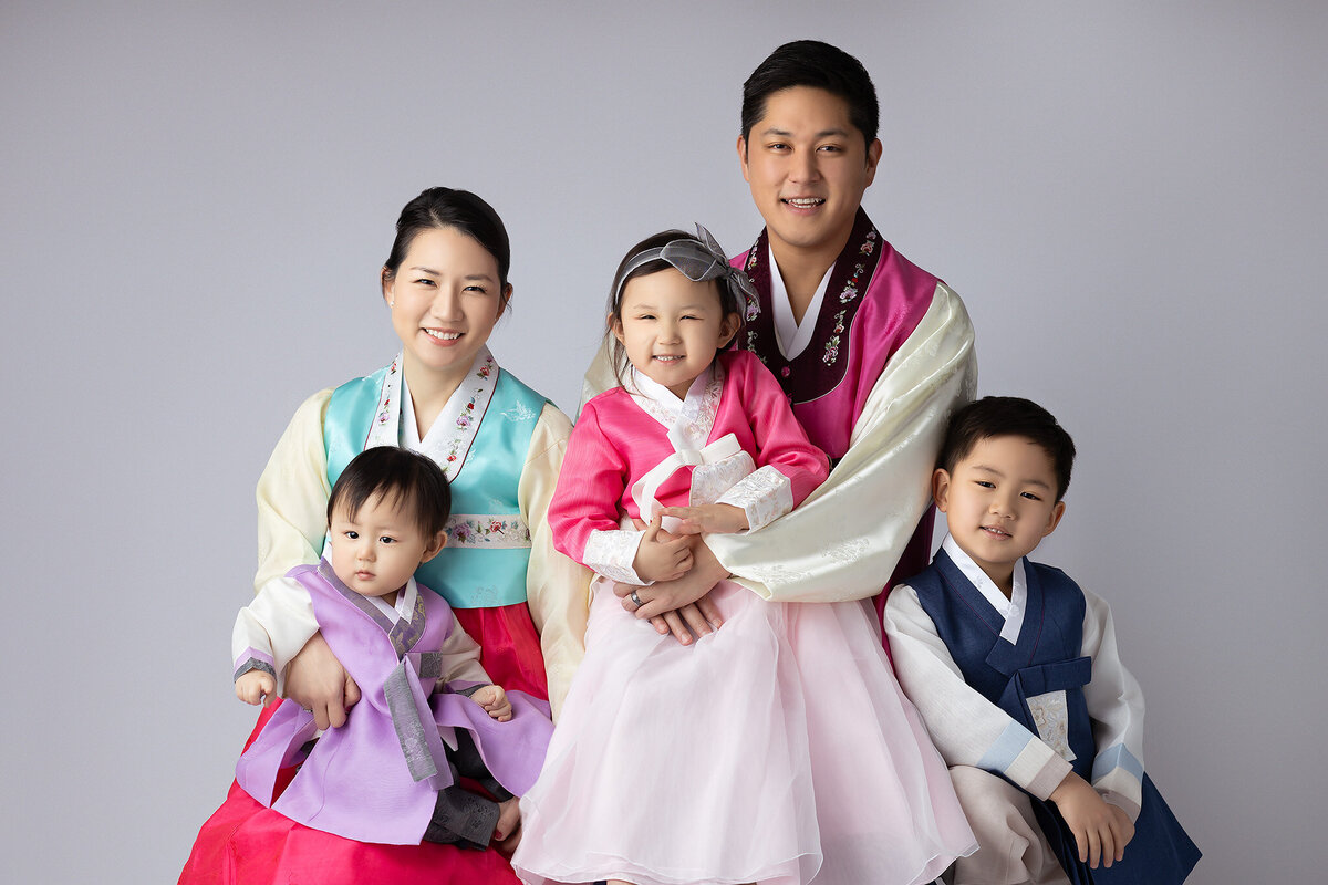 Dallas milestone photographer captures a family of five dressed in traditional Korean Hanbok attire with soft pastel colors against a neutral backdrop.