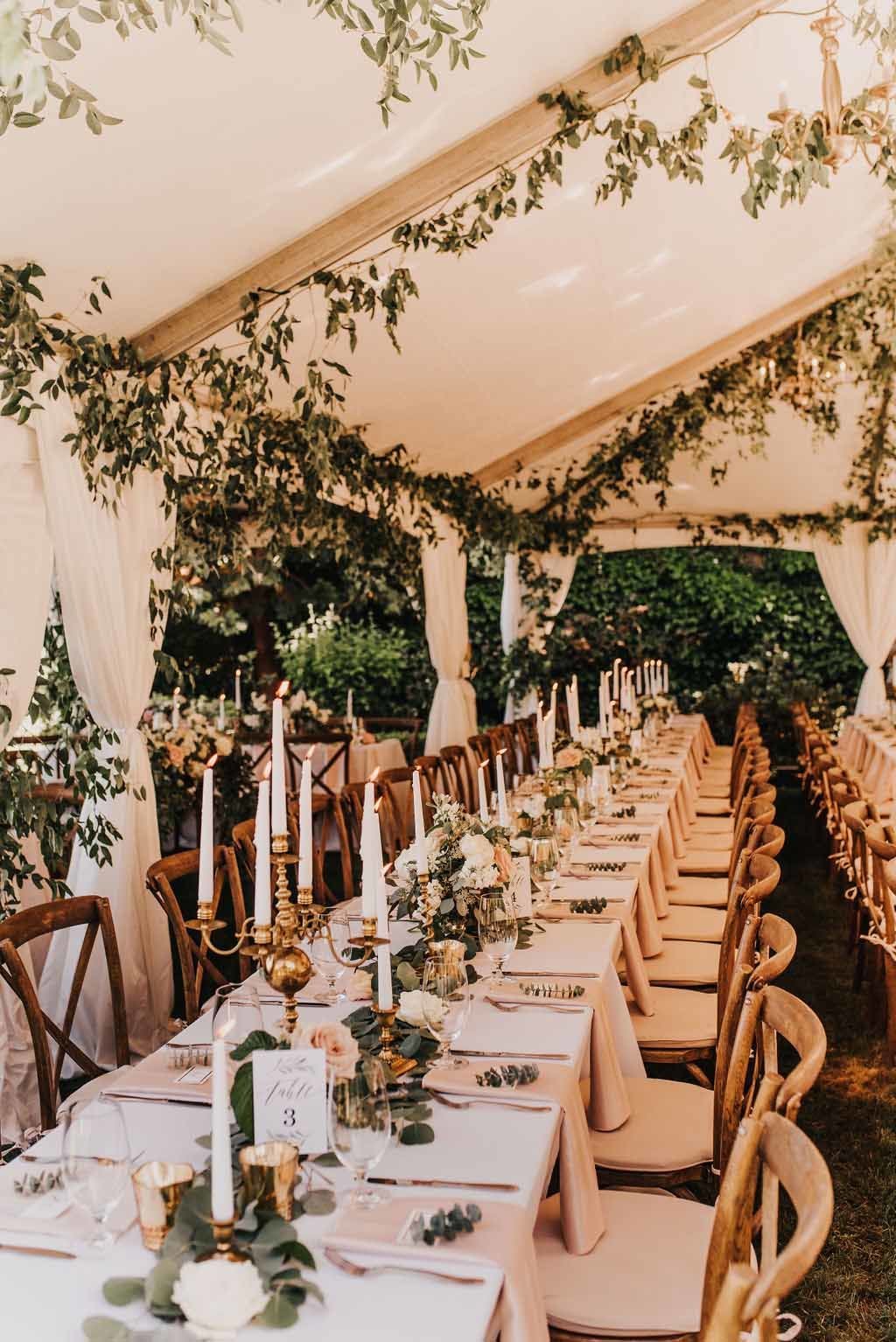 long wedding reception table lined with taper candles, greenery garland runner, and flower blooms, vineyard chairs