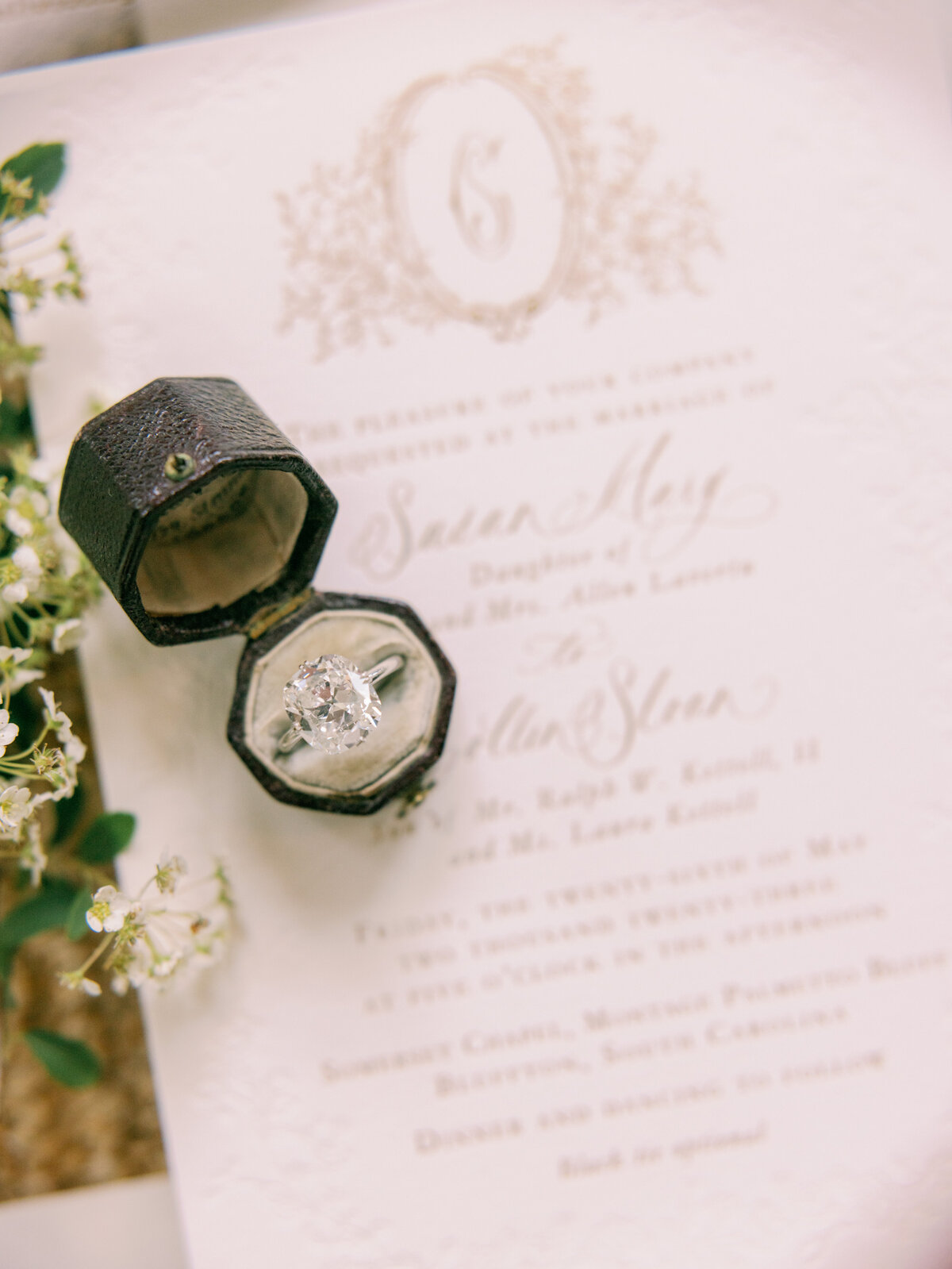 A ring sits in a vintage ring box on top of a couples invitation suite