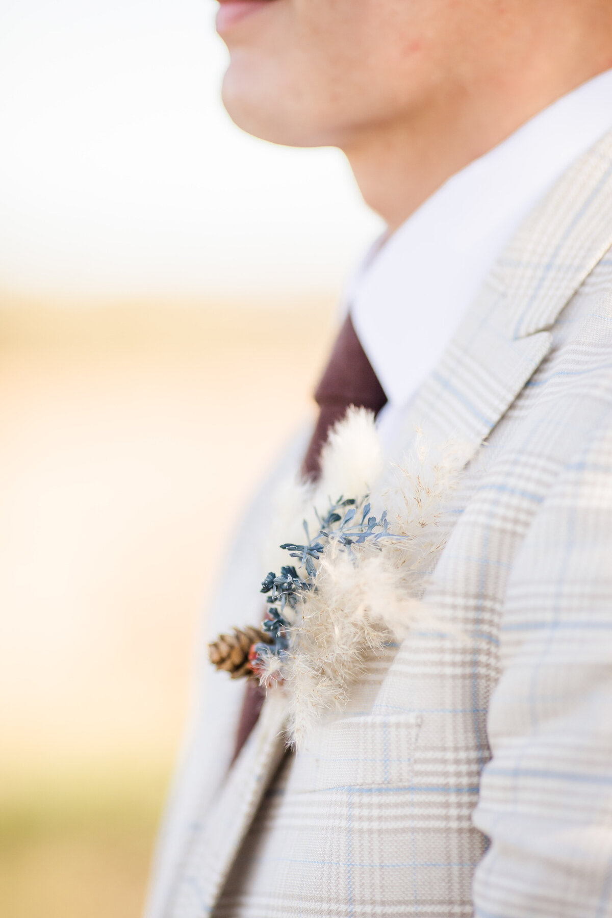 Photo of detail of Grooms subtly striped suit in cream and blue with boutonniere made of pampas grass and dried flowers