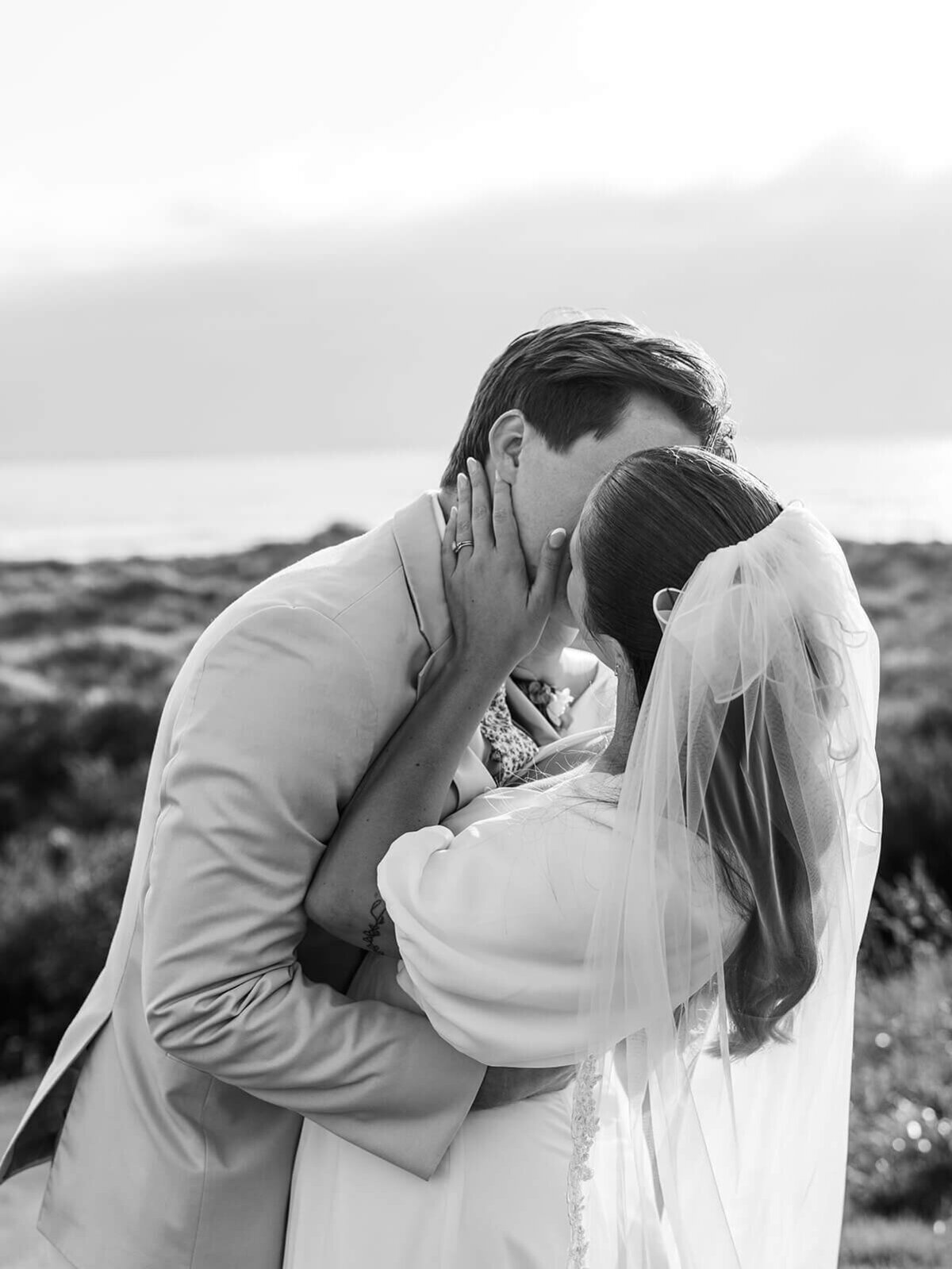 A black and white image of a bride and groom kissing.