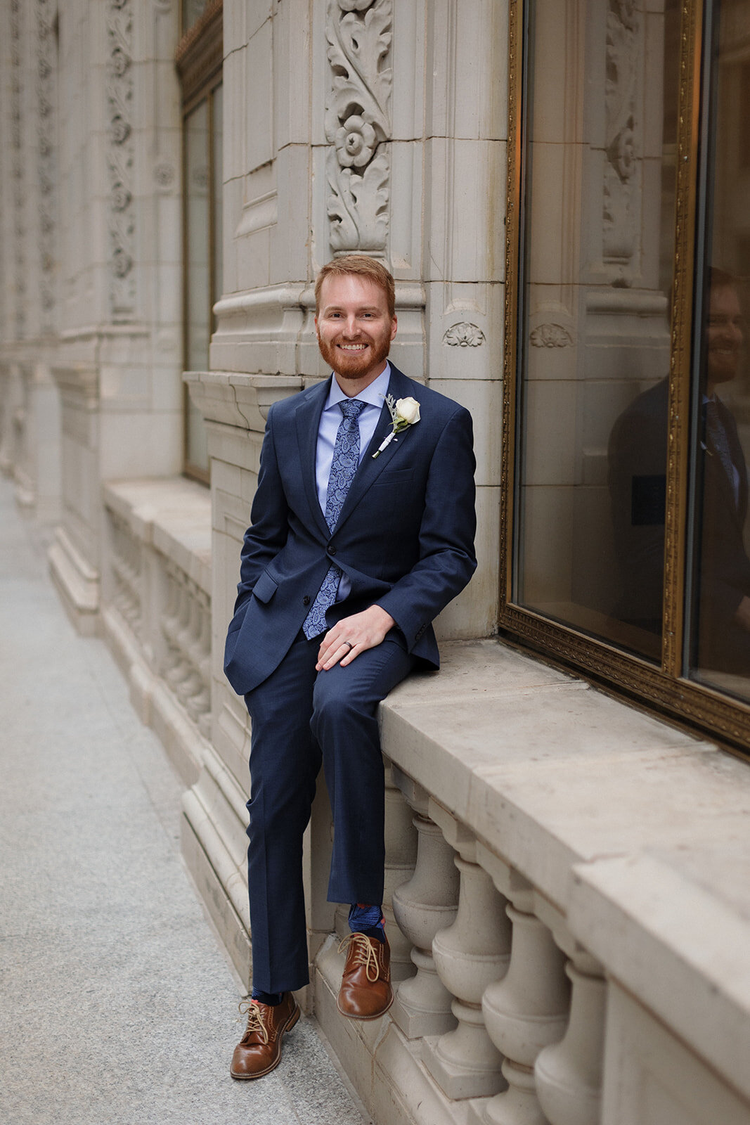 Just Married photo session  groom sitting on ledge on Wrigley Building in Chicago and smiling