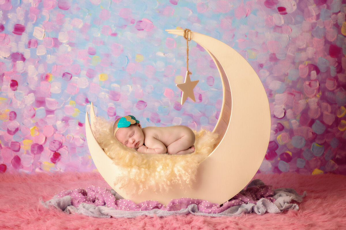 Newborn Photographer, a baby sleeps on a moon prop in a studio with a confetti backdrop