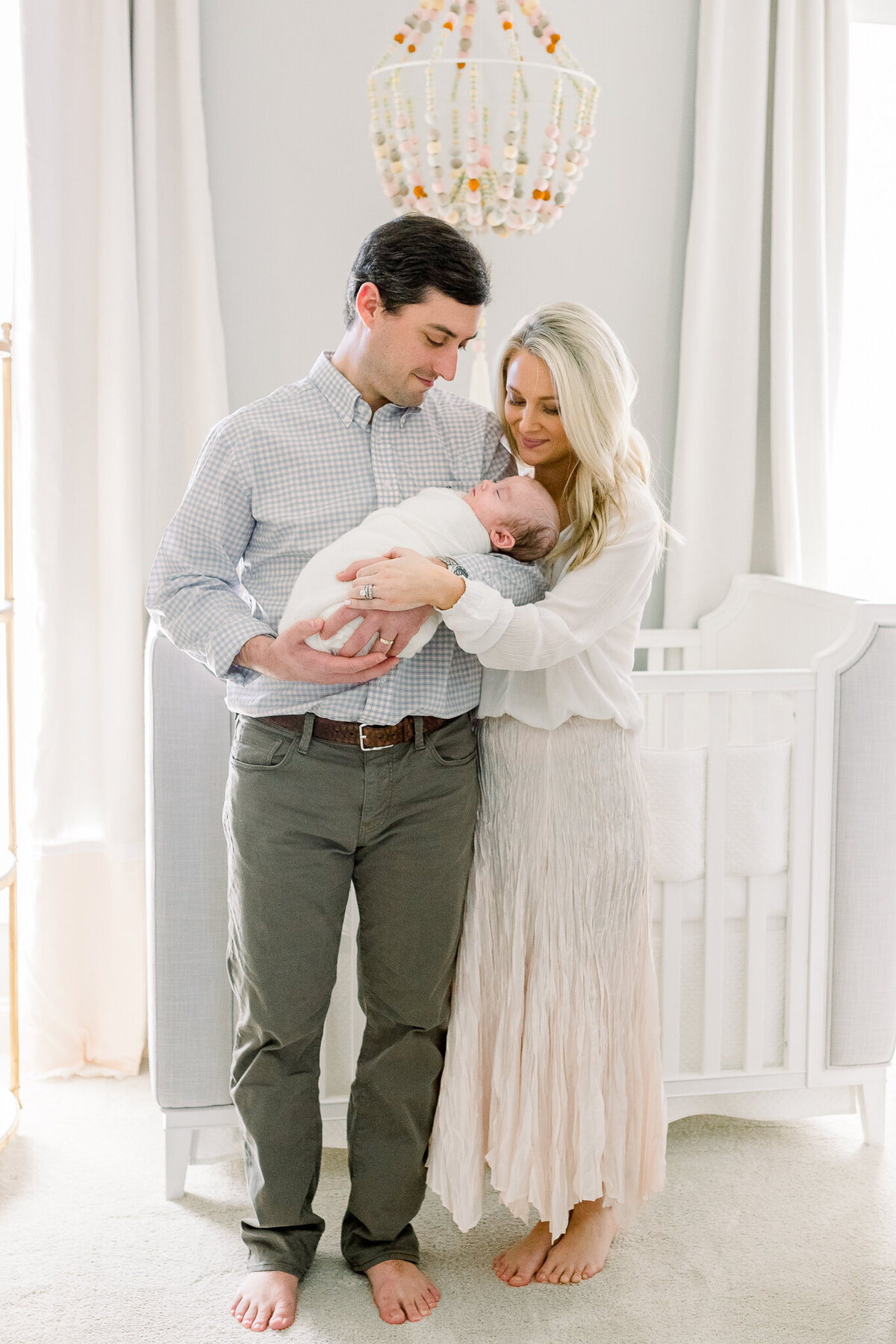 In home newborn session in baby's nursery. Dad is holding swaddled baby girl with mom next to him holding baby girl too. Brandon, MS Newborn Photographer, CJ and Olive Photography.