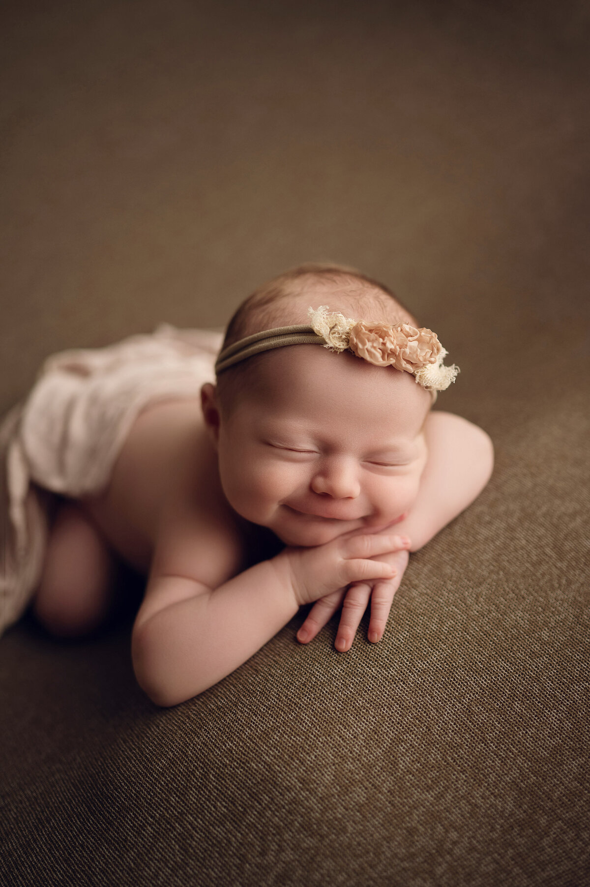 Portrait of smiling, sleeping newborn baby girl wearing a boho floral headband in our metro-Milwaukee studio.