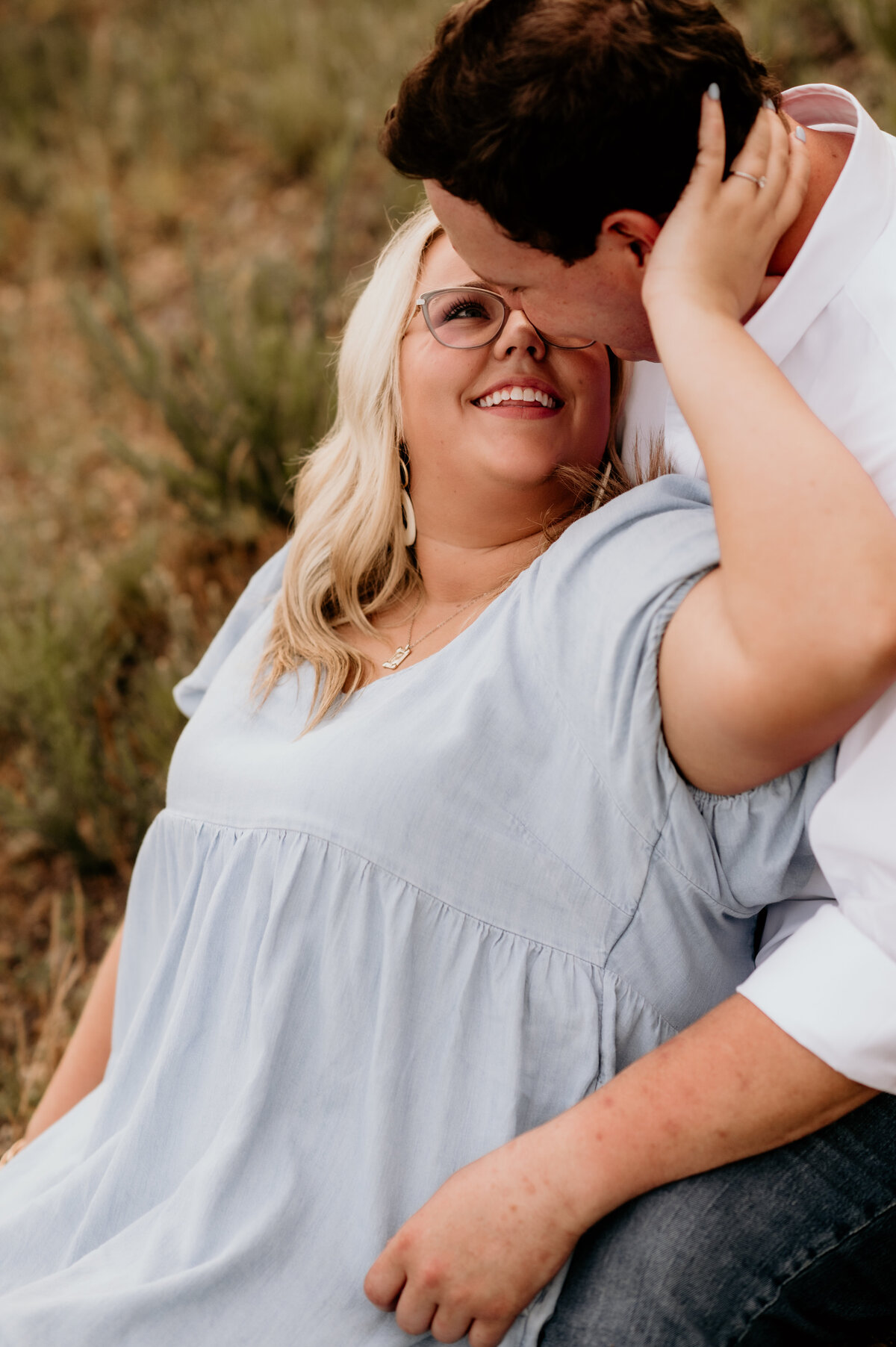 outdoor engagement session with woman sitting in mans lap and holding his face as she looks back at him