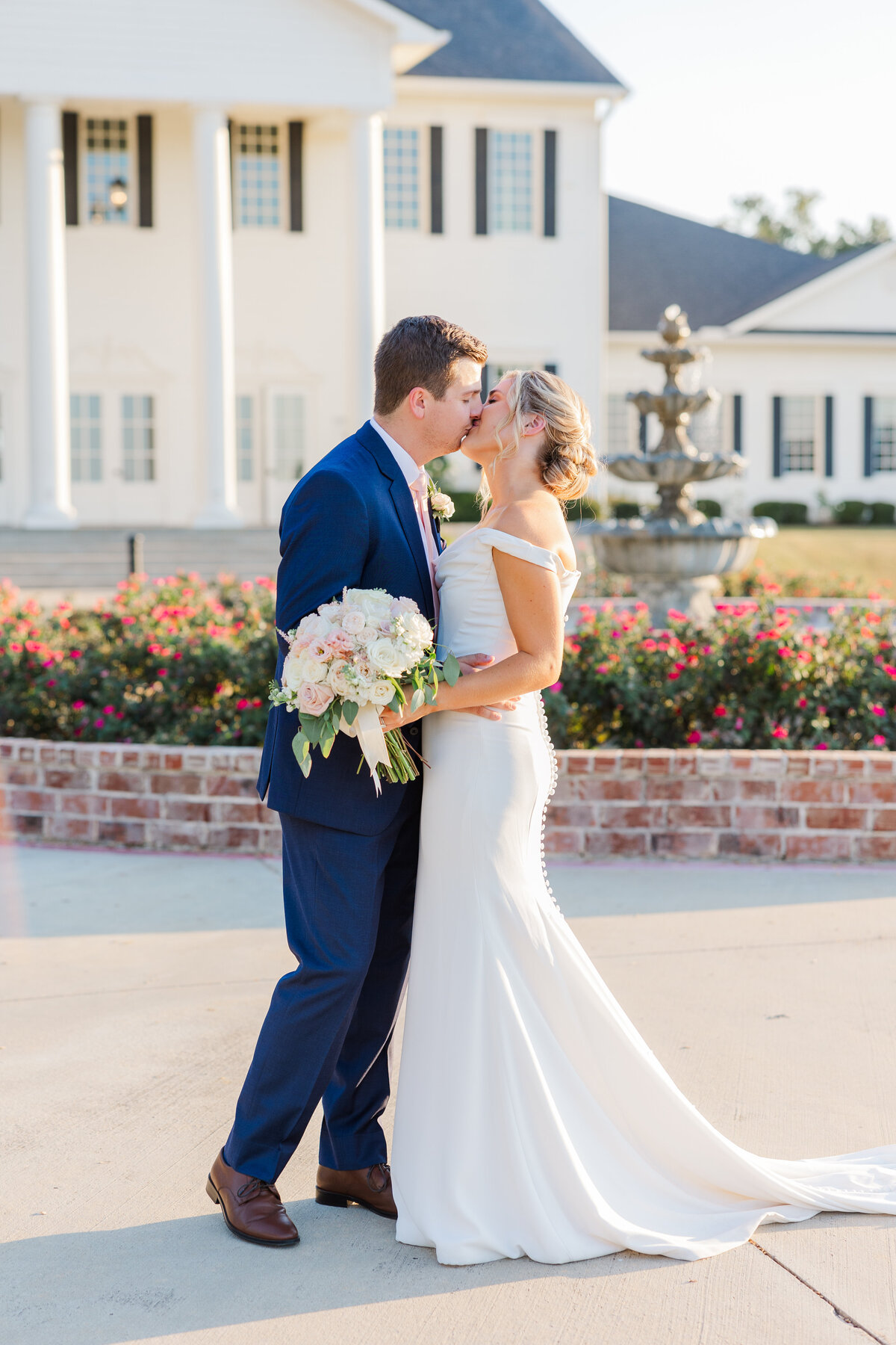 A romantic kiss framed by rose gardens and timeless architecture, showcasing a light and airy wedding style. Ideal for couples looking for luxury DFW wedding photography with classic Southern charm near Plano, Frisco, and Flower Mound.