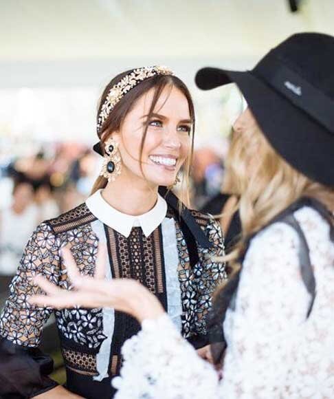 Two elegantly dressed women smiling and talking at the Melbourne Cup Carnival, showcasing race day fashion and headpieces