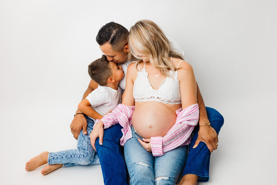A family sits on the ground in the white photography studio and cuddle together.